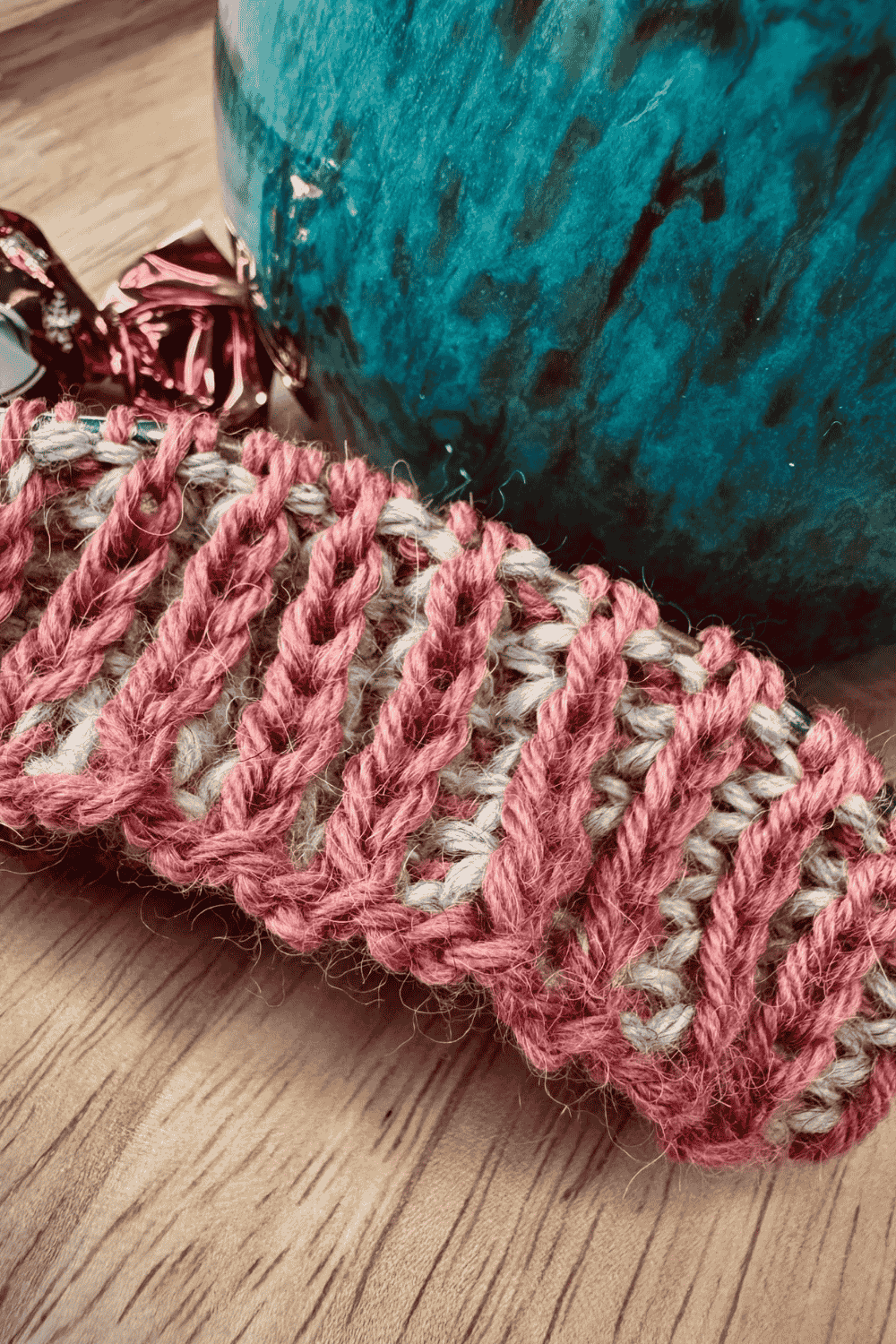 Bündchen mit zweifarbigen Patentmuster in den Farben Altrosa und Hellgrau, mit blauer Tasse auf Holztisch