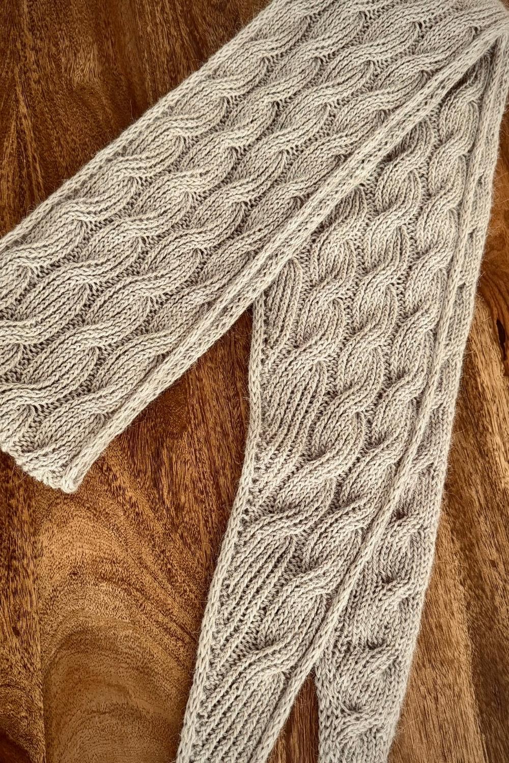 Handgestrickter Minischal Wanderdüne auf Holztisch ausgebreitet, um das plastische Zopfmuster gut sehen zu können
