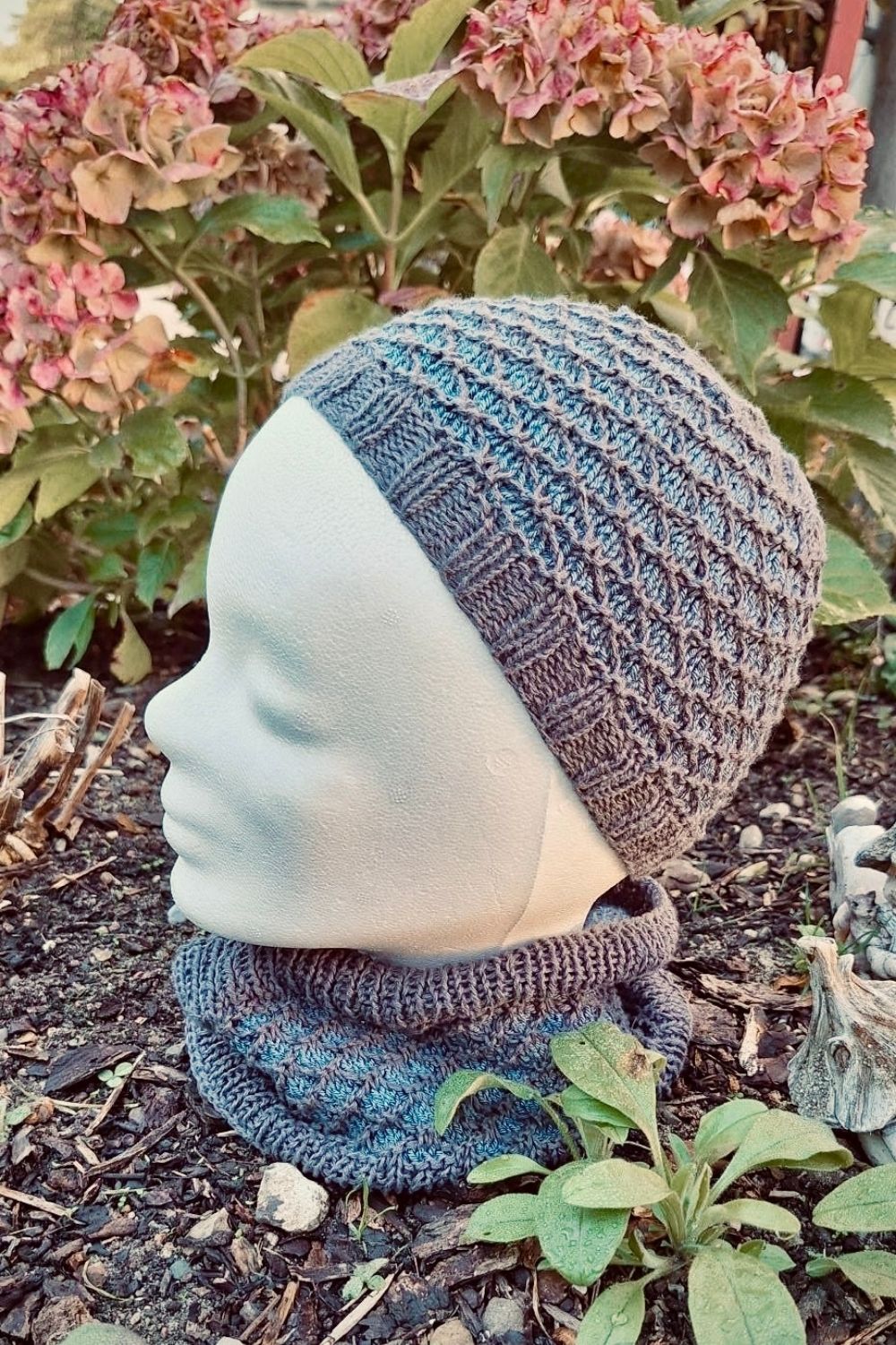 Strickset Dünenwind: Loop und Schal in den Farben Dunkelblau und Hellblau, im Garten fotografiert mit Rhododendron im Hintergrund