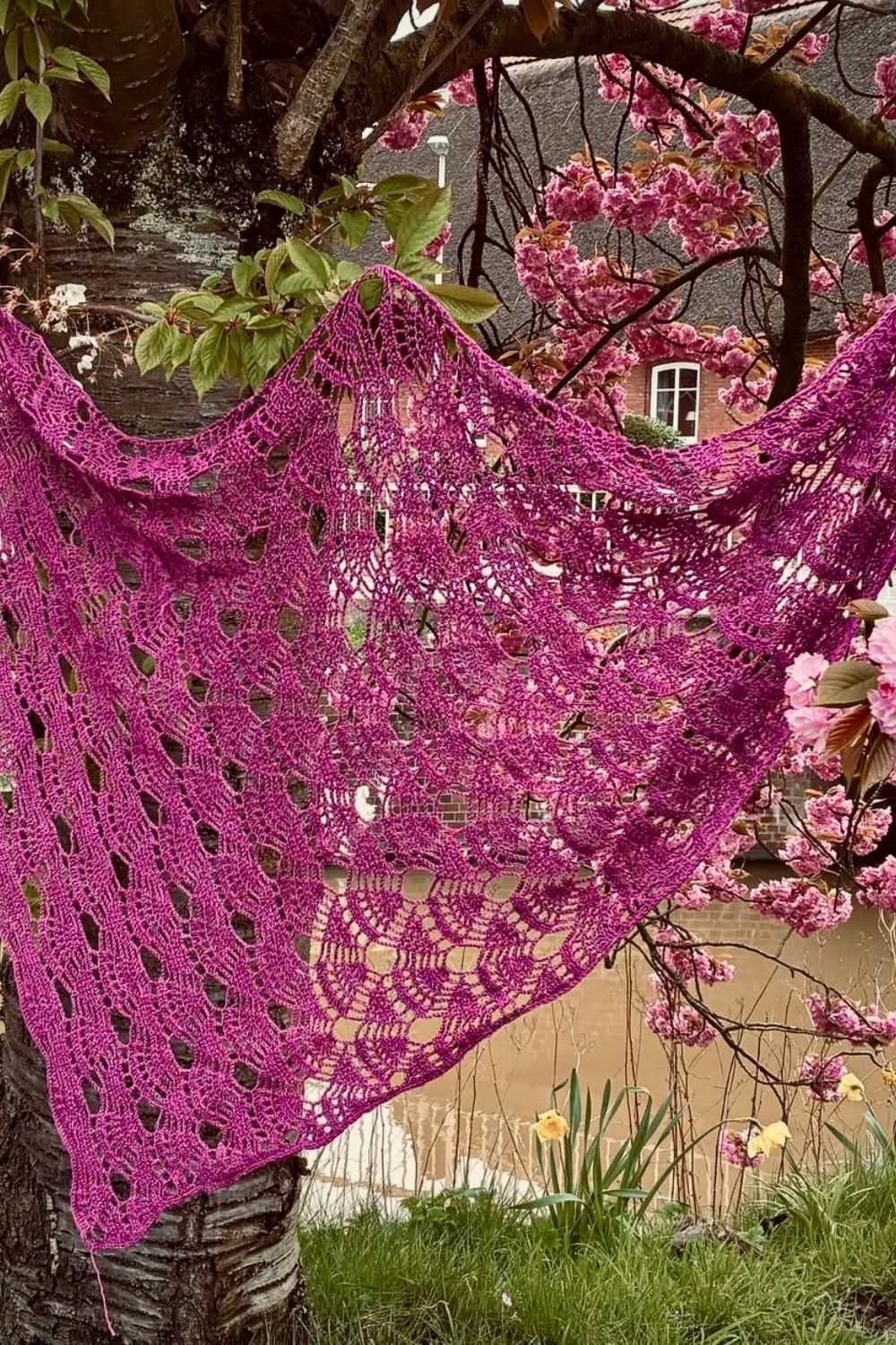 Tuch Akari hängt am Baum, mit Fokus auf das gleichmäßige luftige Muster, gehäkelt aus pinken Garn