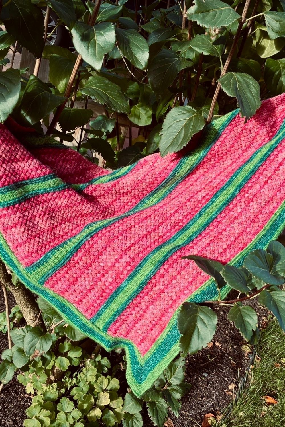 Tuch Flechtwerk in Pink- und Grüntönen unter einem Baum ausgebreitet mit Fokus auf das Flechtmuster