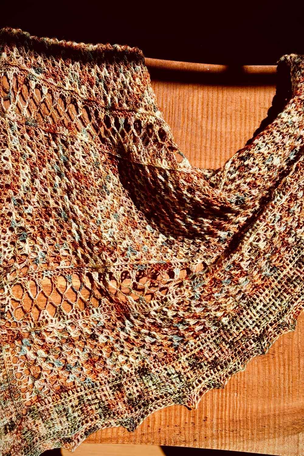 Tuch Komorebi aus bunter Wolle gestrickt, ueber Holzzaun gelegt
