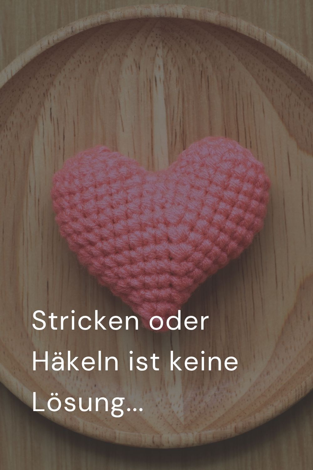 Nahaufnahme von einem gehäkelten Herz auf Holzteller mit Text: Stricken oder Häkeln ist keine Lösung...