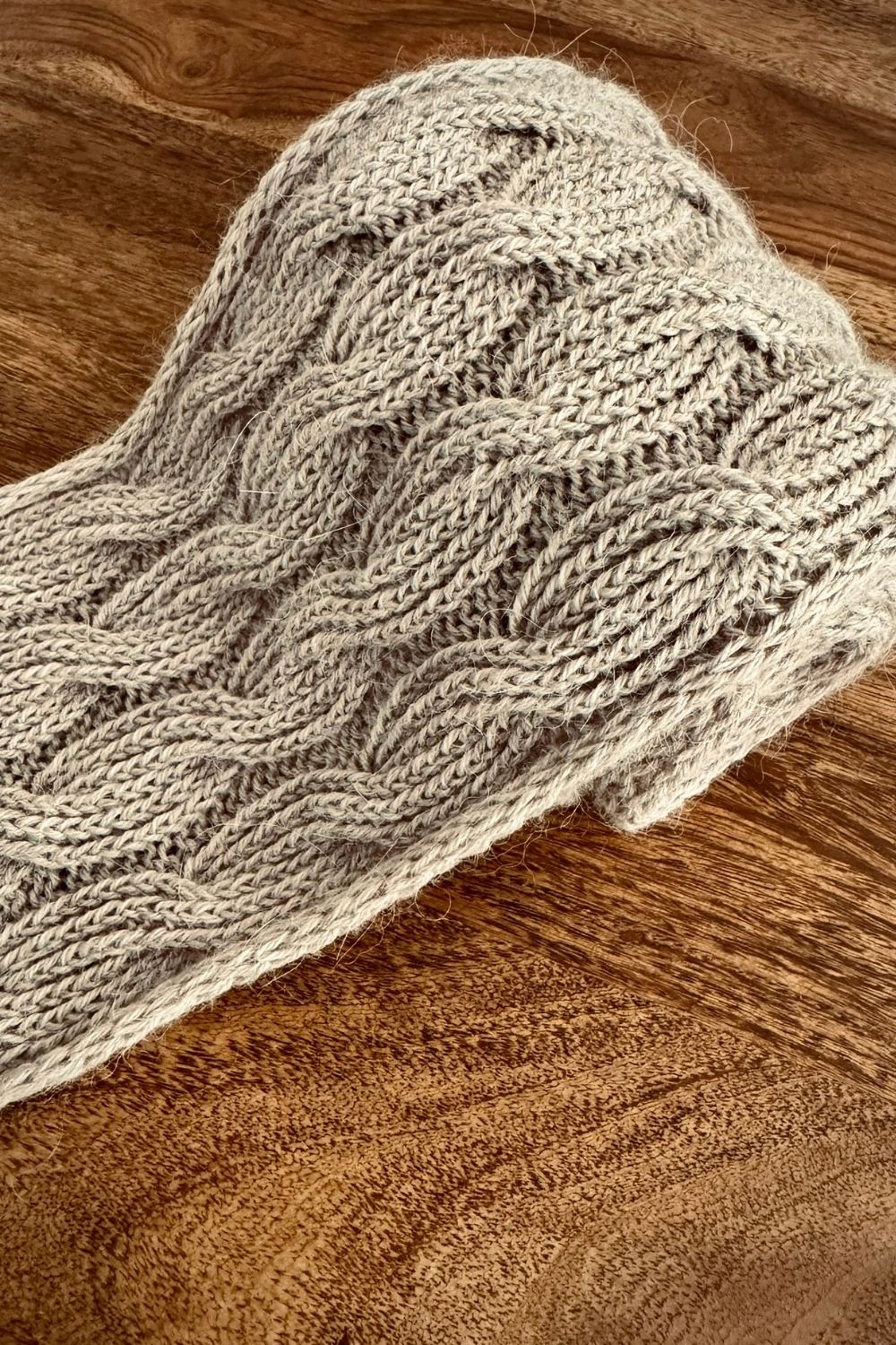 Handgestrickter Minischal Wanderdüne zusammengerollt auf Holztisch, der Fokus liegt auf der Breite des Schals
