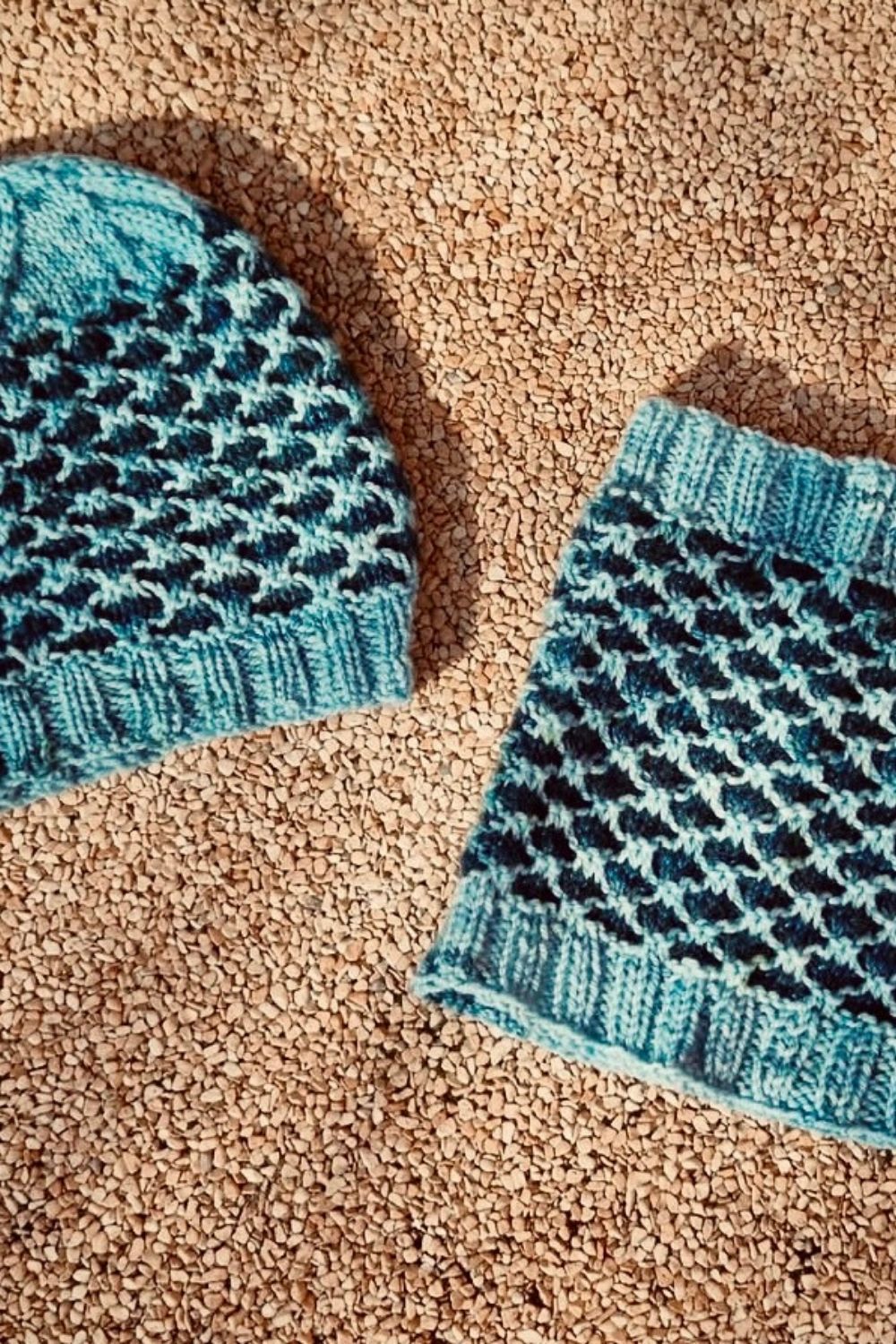 Strickset Dünenwind: Loop und Mütze in den Farben Türkis und Dunkelblau liegen auf dem Boden, Fokus auf das Muster