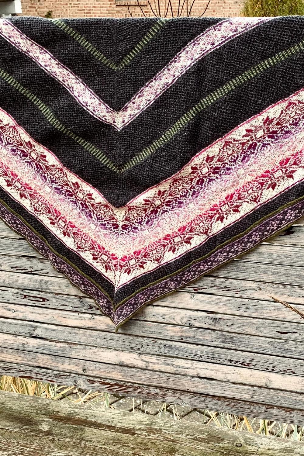 Stricktuch Fairy Glen mit Strukturmuster und mehrfarbigen Muster (Fair Isle) hängt über Holzzaun um das gesamte Muster zu sehen