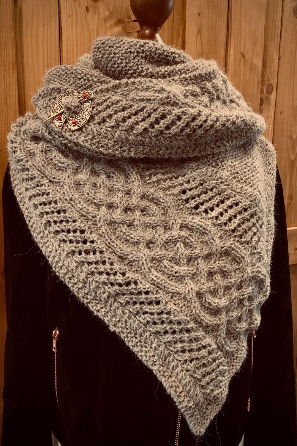 Stricktuch Celtic Mystery mit keltischem Zopfmuster mit einer schwarzen Lederjacke vor einer rustikalen Holzschiebetür präsentiert