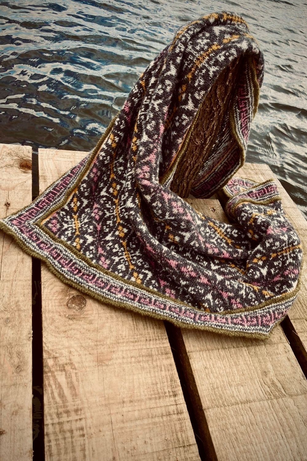 Tuch Kogarashi mit mehrfarbigen Muster (Fair Isle) auf einem Steg, im Hintergund der See