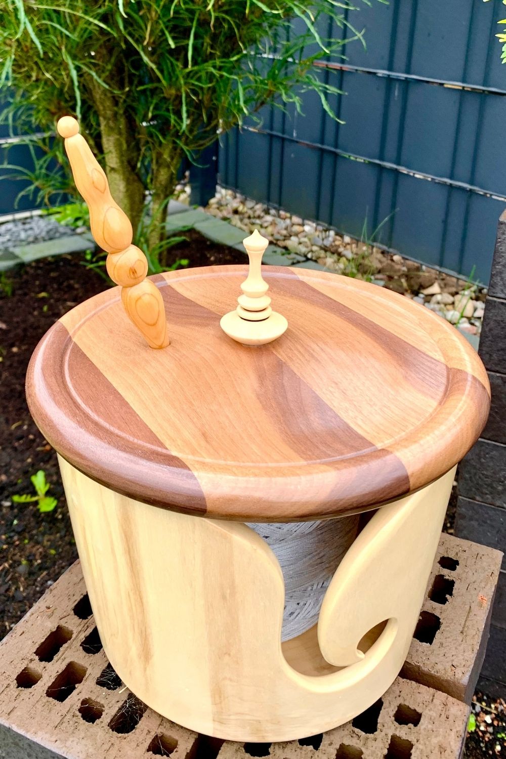 Garnschale mit Deckel und Nadelparkplatz steht im Garten, im Hintergrund Blumenbeet und Bäume